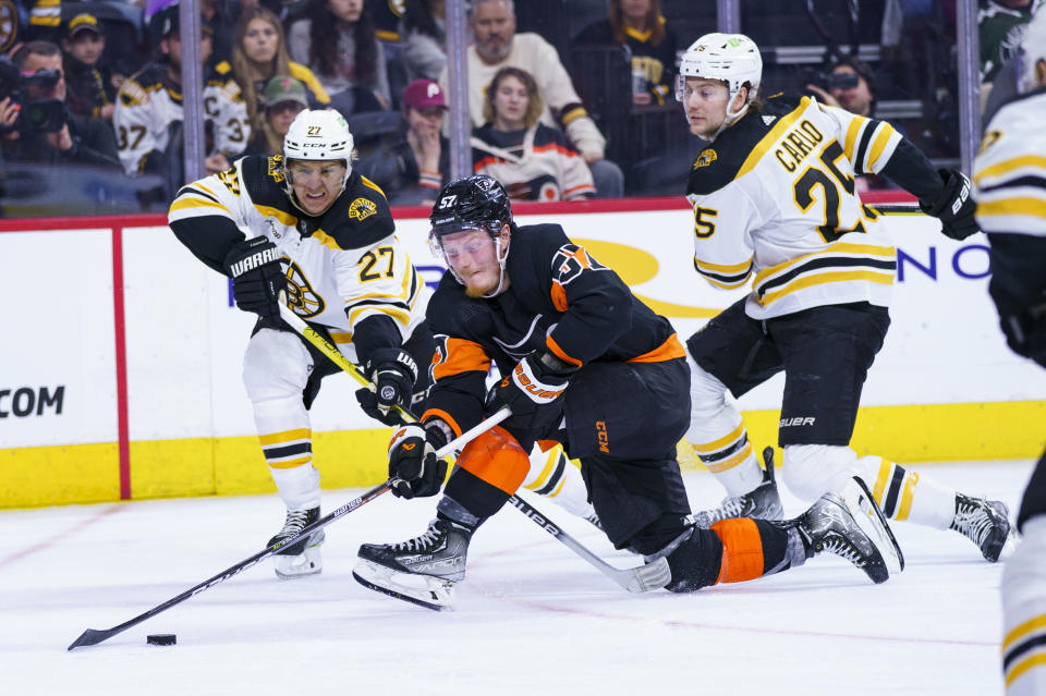 Philadelphia Flyers' Wade Allison, center, battles for the puck against Boston Bruins' Hampus Lindholm, left, and Brandon Carlo, right, during the second period of an NHL hockey game, Sunday, April 9, 2023, in Philadelphia. (AP Photo/Chris Szagola)