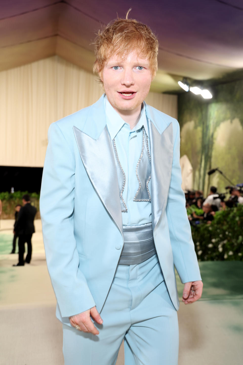 Ed Sheeran at a formal event, wearing a light suit with a metallic tie and a wide waistband