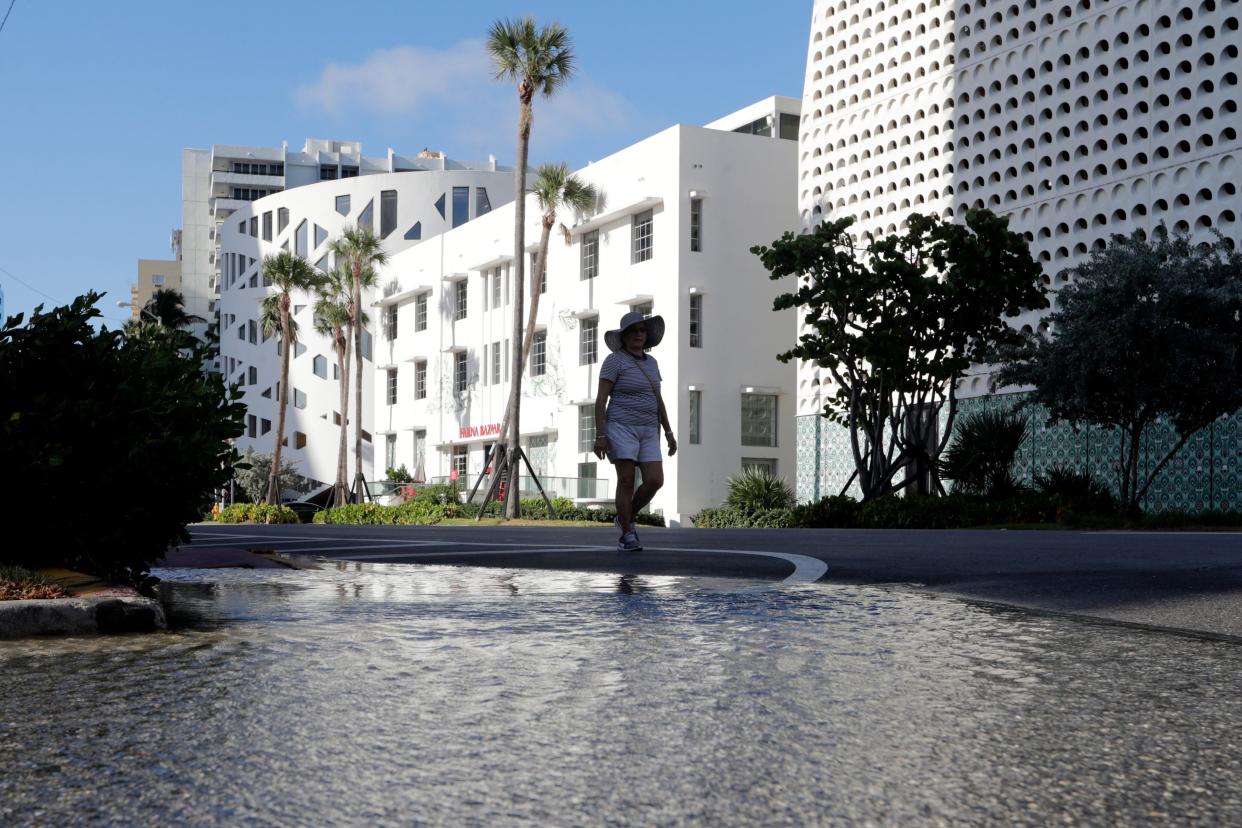A woman walks along a flooded street caused by a king tide in Miami Beach in 2019. Florida  is America’s poster child for climate impacts with tidal flooding, extreme heat, stronger hurricanes and dying coral reefs.