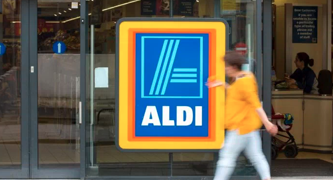 A woman wearing yellow walks past an ALDI supermarket. 