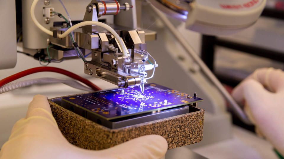 This shot shows a wire bonder being used to attach a silicon chip to a printed circuit board.