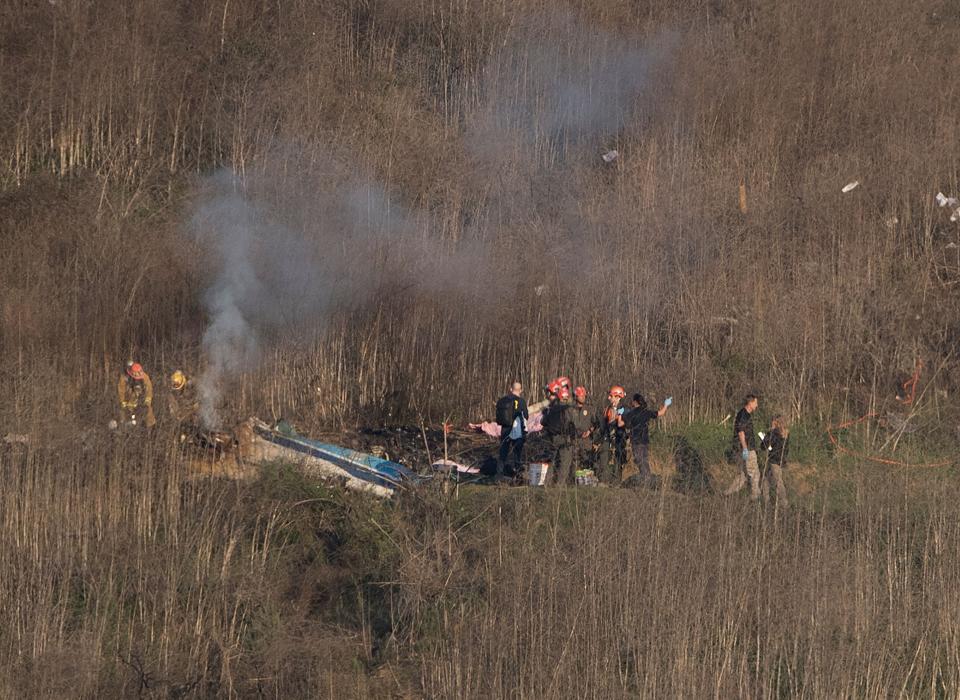 In this file photo taken on January 26, 2020, Los Angeles County Fire Department firefighters and coroner staff check the wreckage at the scene of a helicopter crash in Calabasas.  A court case brought by Kobe Bryant's widow, Vanessa Bryant, over graphic photographs taken by first responders at the site of the helicopter crash that killed him began Aug. 10.