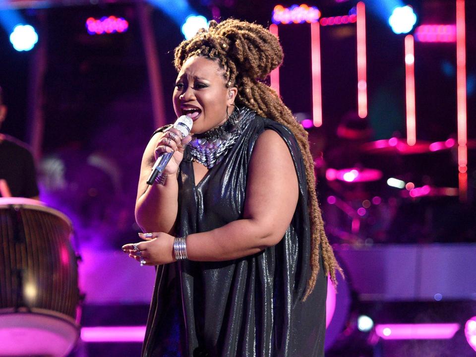 A.S.E., formerly known as La'Porsha Renae, sings and holds a microphone on a stage illuminated with purple light