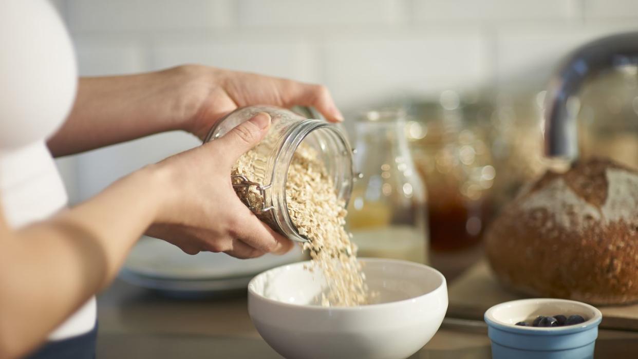 woman pouring oats into bowl in kitchen, close up