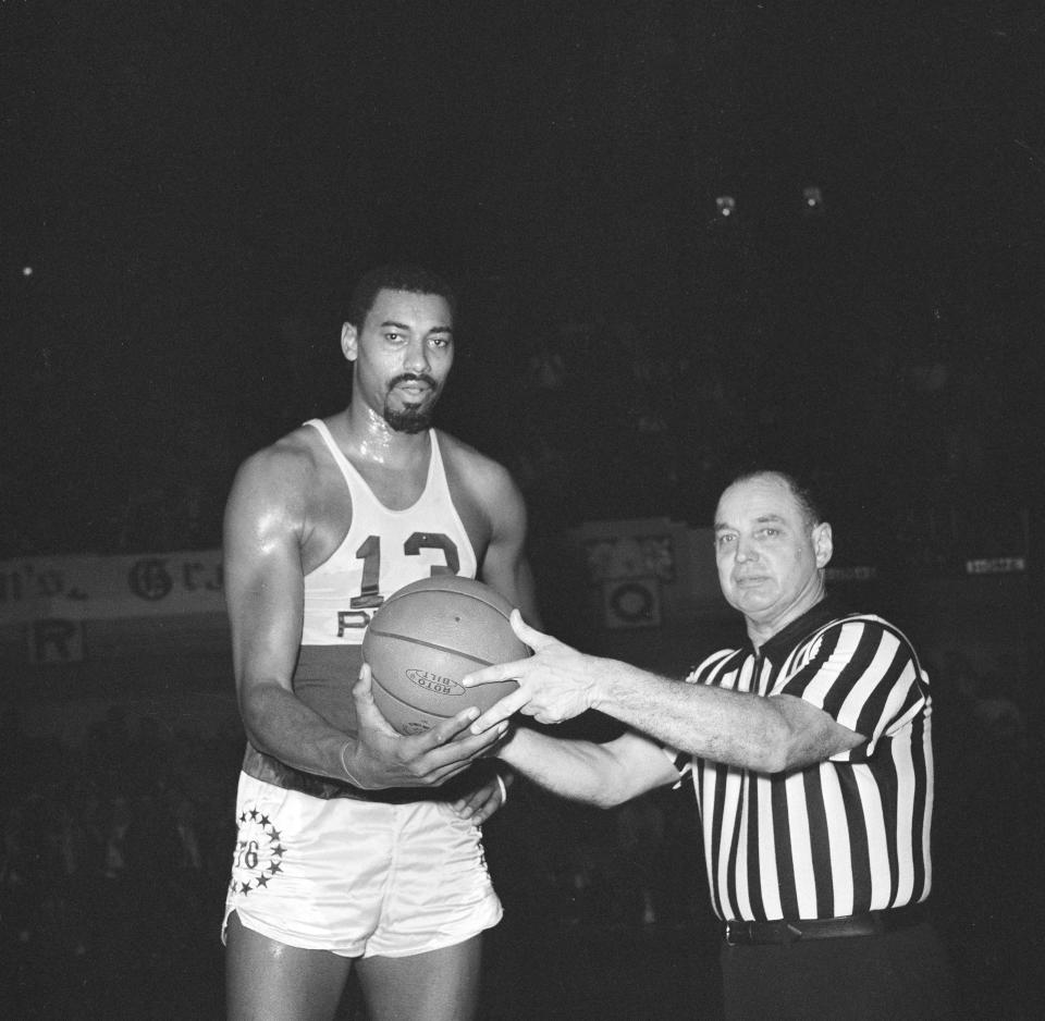 Wilt Chamberlain of the Philadelphia 76ers, who became the second player in the history of the NBA to score 20,000 points, accepts the ball from referee Willie Smith as game with New York Knicks was halted in Philadelphia, Jan. 2, 1965. Presentation was made after Chamberlain sank foul shot for 20,000th point. Chamberlain hopes to surpass the all-time point scoring record of 20,880, held by Bob Pettit, St. Louis Hawks star, before the season ends. 76ers won the game, 133-122.