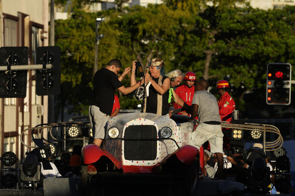 Armandinho Macedo, left center, and Betinho Macedo, sons of Trio Eletrico co-founder Osmar Macedo, are helped with their instruments, as they prepare to participate in a Carnival parade in a replica of their father’s 1929 Ford Model A, in Salvador, Bahia state, Brazil, Sunday, Feb. 4, 2024. In 1950, Osmar, as he is universally known, and his friend Dodô, a radio technician and fellow amateur musician, outfitted the Ford with two speakers and connected their guitar and cavaquinho to the car’s battery, and drove it through the streets to the delight of carnival revelers. (AP Photo/Eraldo Peres)