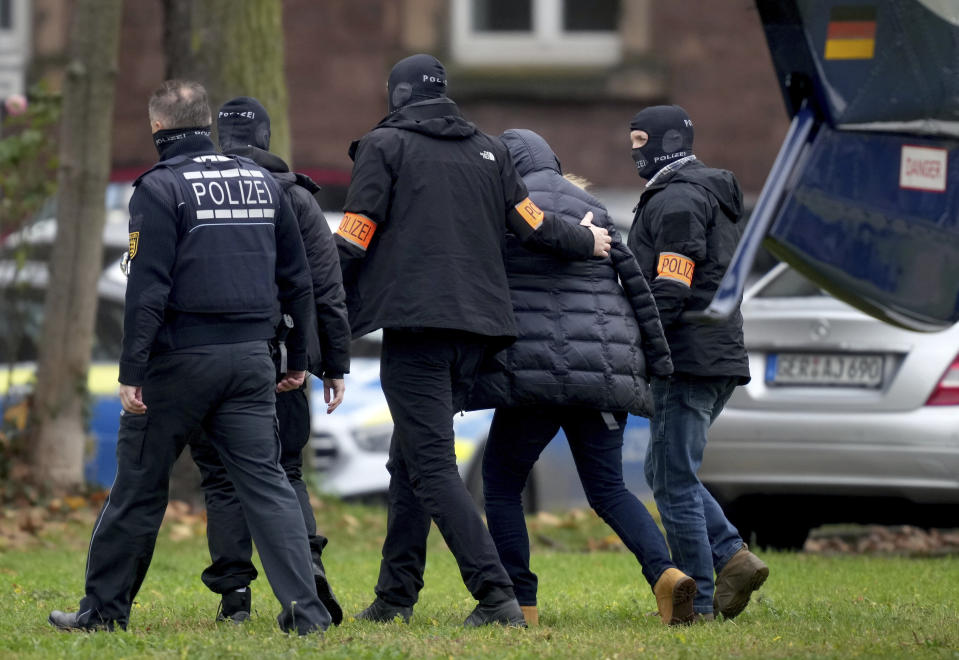 An suspect, second right, is escorted from a police helicopter by police officers after the arrival for a questioning at the federal prosecutor's office in Karlsruhe, Germany, Wednesday, Dec. 7, 2022. Thousands of police officers carried out raids across much of Germany on Wednesday against suspected far-right extremists who allegedly sought to overthrow the government in an armed coup. Officials said 25 people were detained. (AP Photo/Michael Probst)