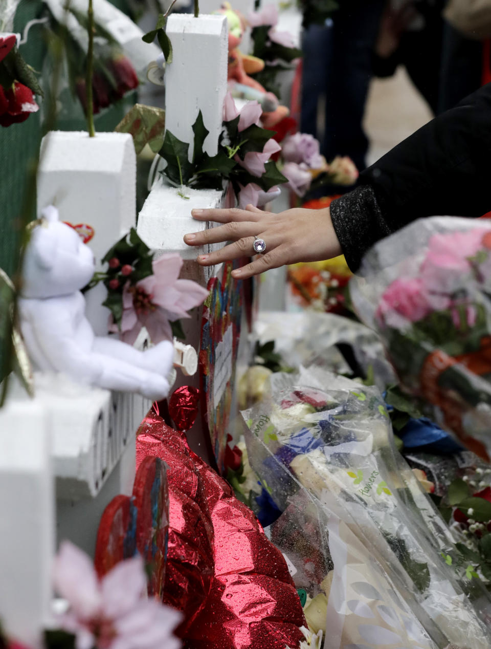 A mourner touches an one of victims' cross at a makeshift memorial Sunday, Feb. 17, 2019, in Aurora, Ill., near Henry Pratt Co. manufacturing company where several were killed on Friday. Authorities say an initial background check five years ago failed to flag an out-of-state felony conviction that would have prevented a man from buying the gun he used in the mass shooting in Aurora. (AP Photo/Nam Y. Huh)