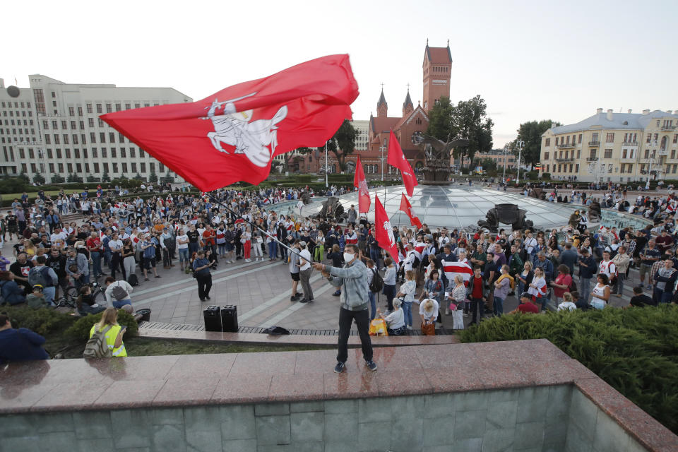 A protester waves a flag with an old Belarusian national emblem during an opposition rally at Independent Square in Minsk, Belarus, Monday, Aug. 24, 2020. Belarusian authorities on Monday detained three leading opposition activists who have helped spearhead a wave of protests demanding the resignation of the country's authoritarian president Alexander Lukashenko following a disputed election. (AP Photo/Dmitri Lovetsky)