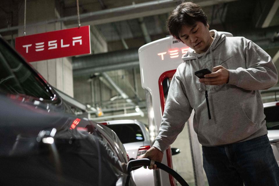 This photo taken on January 27, 2023 shows Atsushi Ikeda, the founder and vice president of a Japanese club for Tesla owners, checking his phone as he charges his Tesla Model S at a charging station in Tokyo. - Last year, 59,000 new EVs were sold in Japan, a record and a three-fold annual increase, but still less than two percent of sales of all cars in the country in 2022