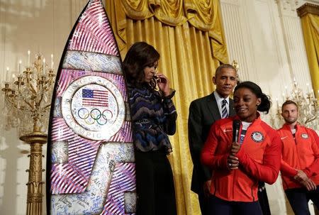 2016 Olympic individual all-around gymnast Simone Arianne Biles presents a surf board to U.S. President Barack Obama and First lady Michelle Obama as he welcomes U.S. Olympic and Paralympics teams at the White House in Washington, U.S., September 29, 2016. REUTERS/Yuri Gripas