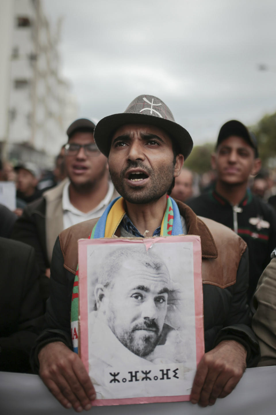 A protester holds a photo of Hirak leader Nasser Zefzafi during a demonstration in Rabat, Morocco, Sunday, April 21, 2019. Protesters are condemning prison terms for the leader of the Hirak Rif protest movement against poverty and dozens of other activists. Banner in Berber reads Zefzafi's name. (AP Photo/Mosa'ab Elshamy)