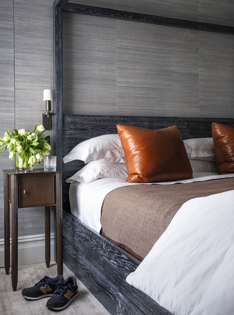 bed with gray wood panel wall behind, black frame, and camel leather pillows