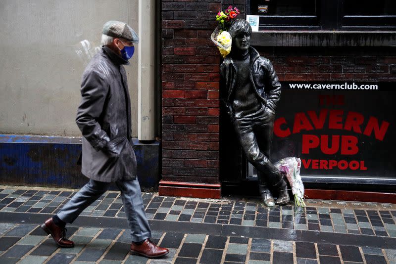 A man wearing a face mask walks past John Lennon statue in Liverpool