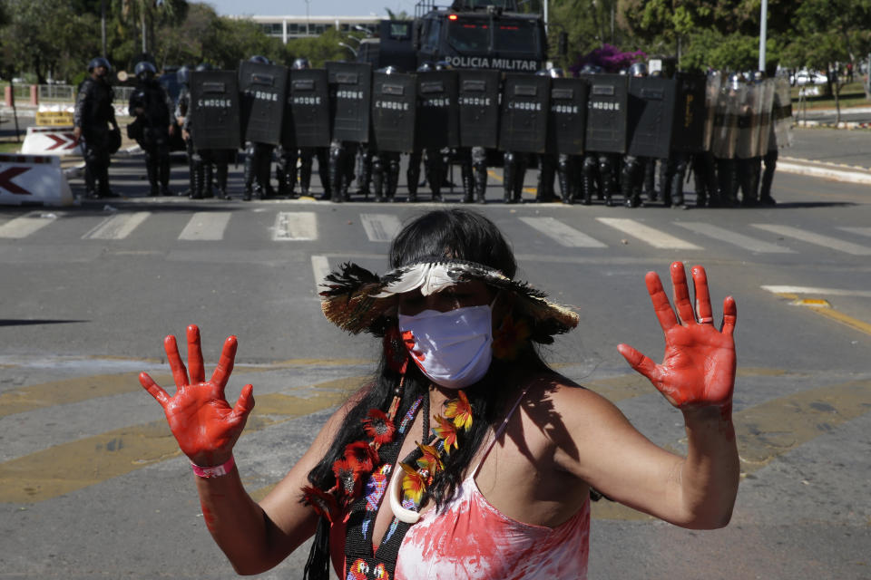 An Indigenous woman stands in front of a formation of riot police blocking a road, outside Congress in Brasilia, Brazil, Tuesday, June 22, 2021. Indigenous are camping in the capital to oppose a proposed bill they say would limit recognition of reservation lands. (AP Photo/Eraldo Peres)