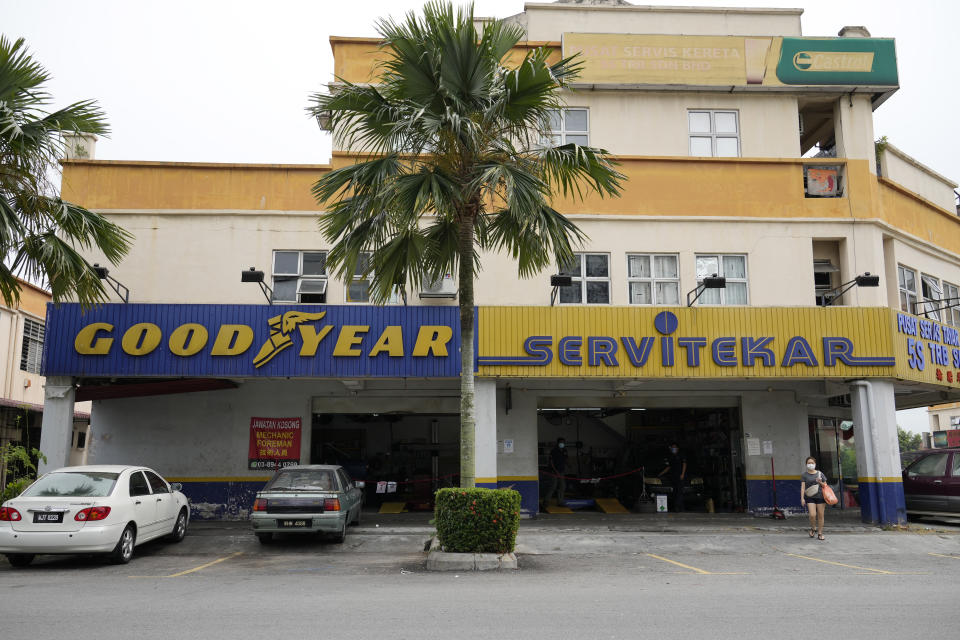 A woman wearing a face mask walks near a Goodyear shop in Bukit Jalil, outskirts of Kuala Lumpur, Malaysia, Friday, June 11, 2021. A Malaysian court on Thursday ruled in favor of 65 migrant workers who sued U.S. tiremaker Goodyear for underpaying them, their lawyer said, calling it a victory for foreign employees. (AP Photo/Vincent Thian)