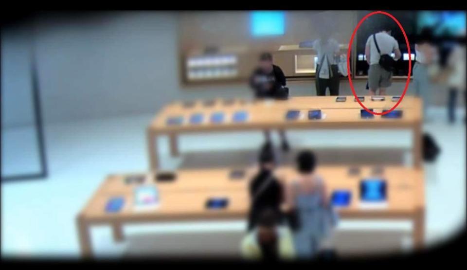 許男（紅圈）到信義區的蘋果專賣店佯裝購物，趁隙將架上耳機偷走放入背包內。（翻攝畫面）