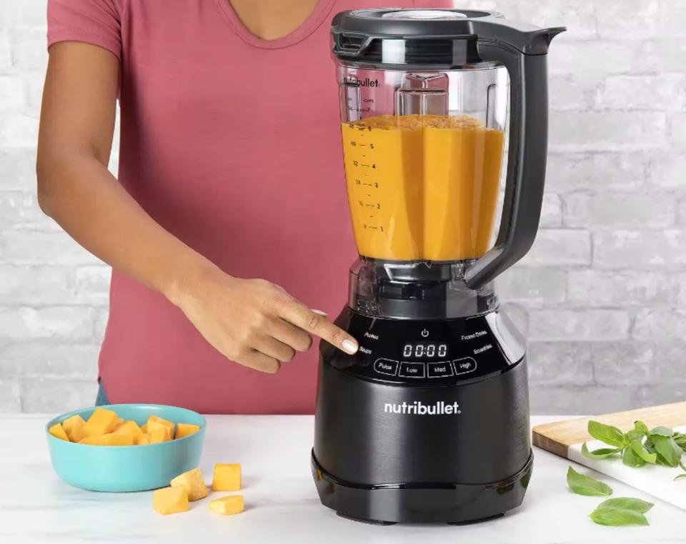  A Nutribullet Smart Touch Blender in a kitchen. A woman is using it to blend squash for soup 