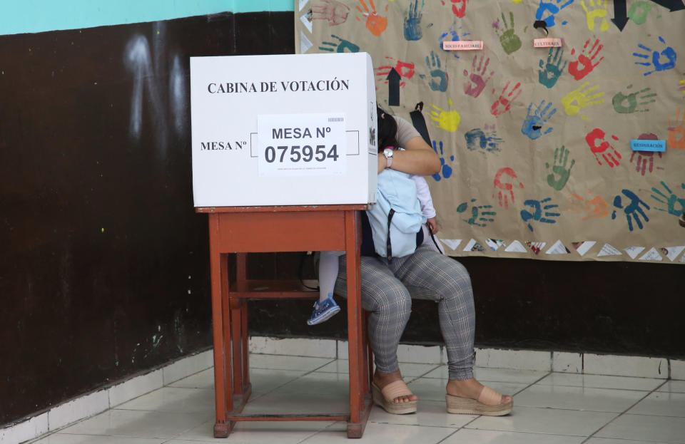 A woman holding a toddler fills in her ballot during a referendum aimed at curbing corruption in Lima, Peru, Sunday, Dec. 9, 2018. The four questions on the ballot include measures that would prohibit legislators from immediate reelection, create stricter campaign finance rules and reform a scandal-tainted council charged with selecting judges (AP Photo/Cesar Olmos)