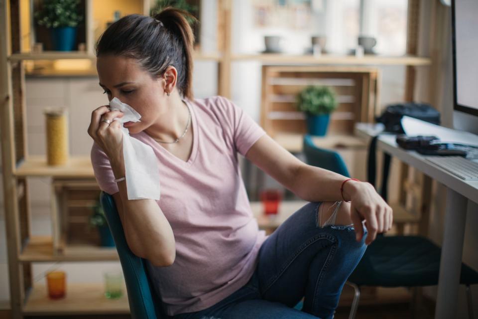 A sitting woman turns in her chair and puts a tissue to her nose.