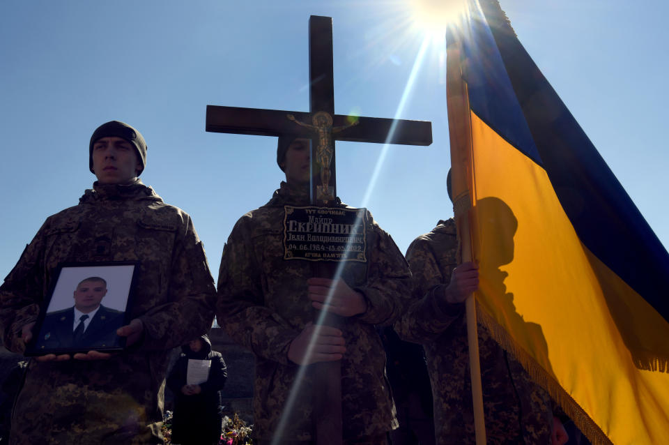 Men dressed in uniform hold a photo of a fallen soldier and the Ukrainian flag.
