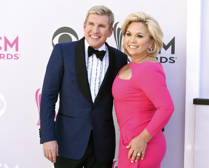 Todd Chrisley in a blue tuxedo and his wife, Julie Chrisley in a pink dress pose for photos