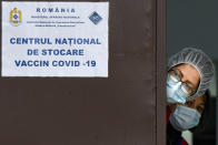 In this photo taken on Friday, Dec. 18, 2020 medical staff wearing masks for protection against the COVID-19 infection peer from behind a door at the National Center for Storage of the COVID-19 Vaccine, a military run facility, in Bucharest, Romania. Across the Balkans and the rest of the nations in the southeastern corner of Europe, a vaccination campaign against the coronavirus is overshadowed by heated political debates or conspiracy theories that threaten to thwart the process. In countries like the Czech Republic, Serbia, Bosnia, Romania and Bulgaria, skeptics have ranged from former presidents to top athletes and doctors. Nations that once routinely went through mass inoculations under Communist leaders are deeply split over whether to take the vaccines at all. (AP Photo/Andreea Alexandru)