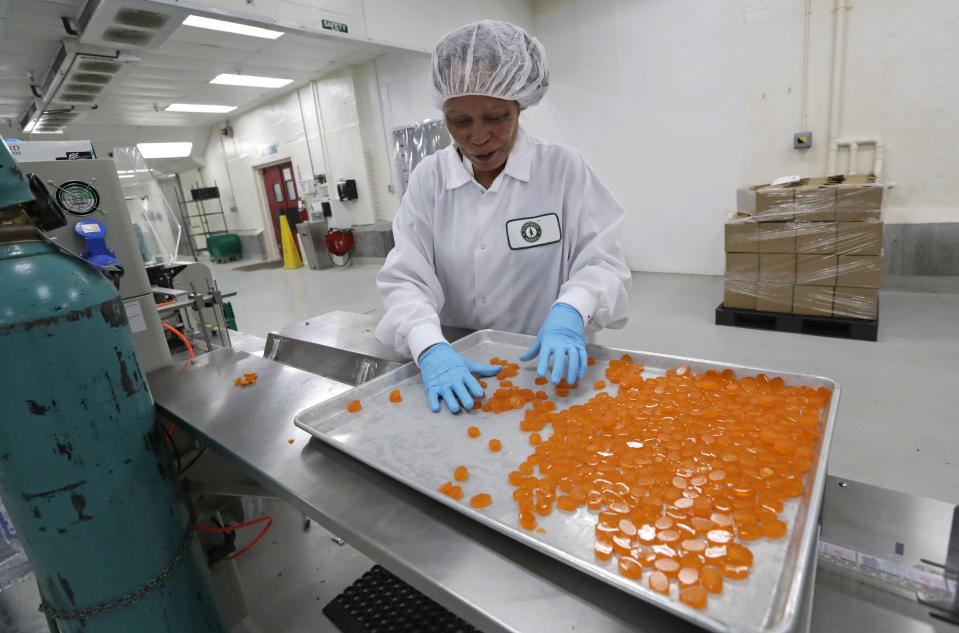 Ioka Tasi works on packaging cannabis-infused mango hard candies at Evergreen Herbal, Wednesday, July 24, 2019, in Seattle. Washington state's marijuana regulators have eased some requirements regarding the "seed to sale" tracking of the drug, a week after a botched software update began preventing many business from being able to ship their products, cost hundreds of thousands of dollars in lost sales and prompted some to furlough workers. (AP Photo/Elaine Thompson)