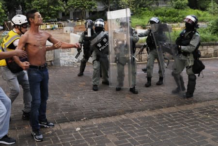 A shirtless anti-government protester is being prevented from confronting riot police officers during a protest at Tai Po district, in Hong Kong