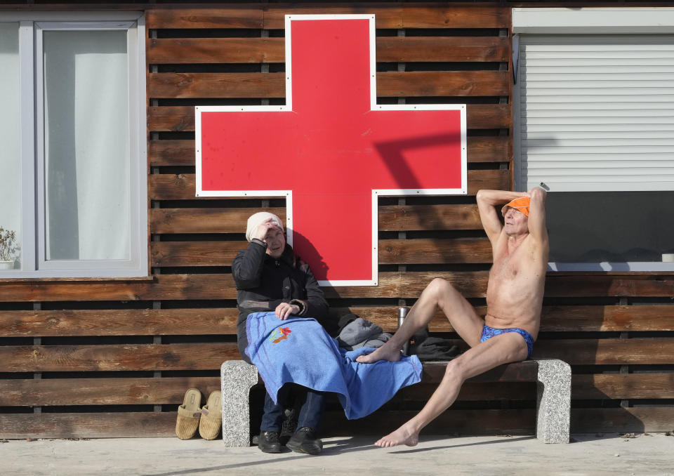 A man sunbathes while a woman in warm clothes looks at him sitting on a bench on a city beach in Kyiv, Ukraine, Sunday, Feb. 20, 2022.(AP Photo/Efrem Lukatsky)