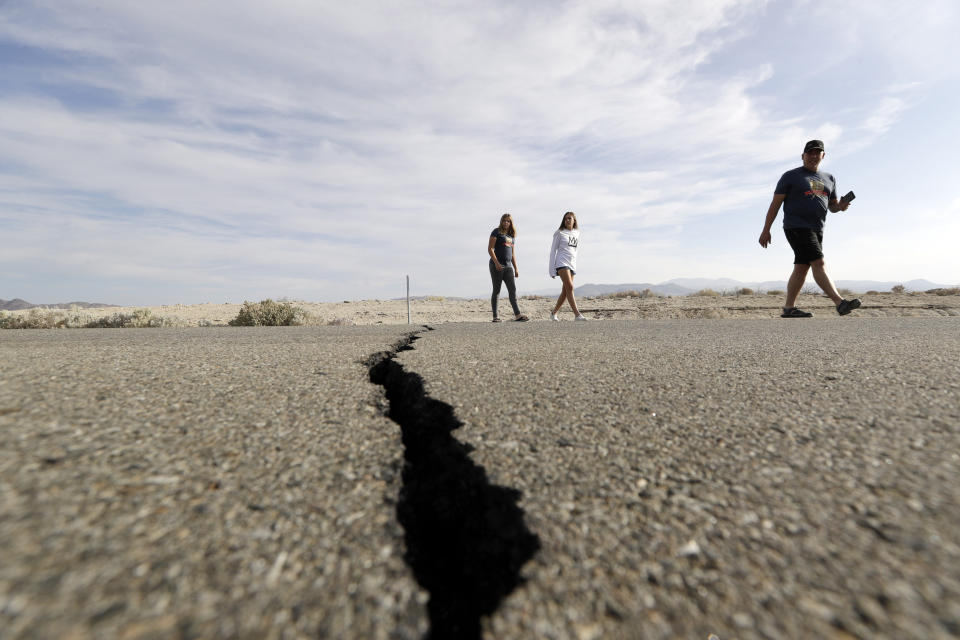 Visitors cross highway 178 next to a crack left on the road by an earthquake Sunday, July 7, 2019, near Ridgecrest, Calif. (AP Photo/Marcio Jose Sanchez)