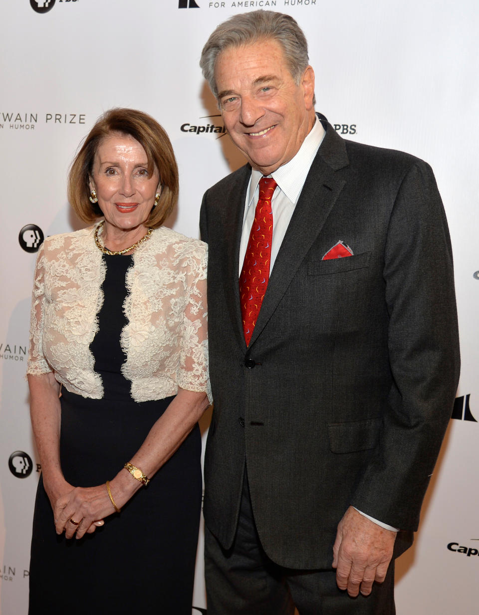 Nancy and Paul Pelosi pose for photographers in front of a red carpet wall carrying names of sponsors of the event, including: the American Fund, Capital and PBS.