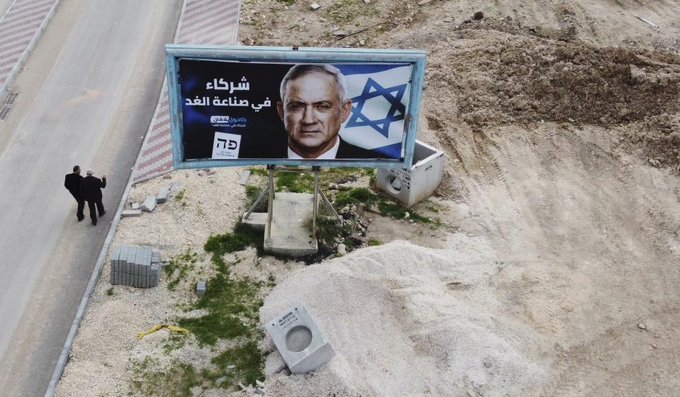 Men walk past an election campaign billboard for Blue and White party leader Benny Gantz, in the Arab town of Baqa al-Gharbiyye, northern Israel, Monday, Feb. 17, 2020. The Arabic reads, "We are partners for tomorrow." (AP Photo/Ariel Schalit)