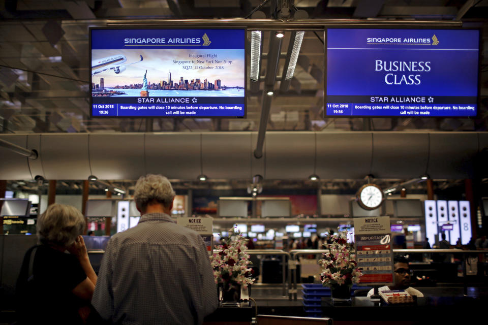 Passengers traveling on Singapore Airlines flights wait at check-in counters where advertisements for the airline's inaugural non-stop flight from Singapore to New York is flashed on screens on Thursday, Oct. 11, 2018, in Singapore. The world's longest flight is taking travelers from Singapore to New York. Operated by Singapore Airlines, the city-state's national carrier, the trip will take less than 19 hours. Skipping a stopover in Frankfurt shaves as much as 6 hours off traveling time, the carrier said. (AP Photo/Wong Maye-E)