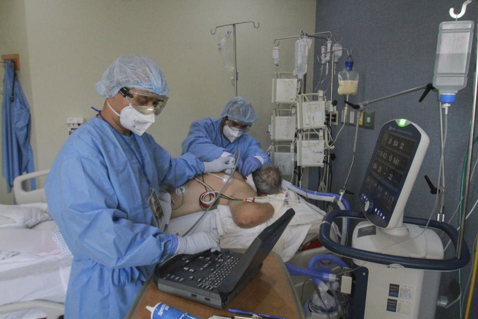 In this May 14, 2020 photo, Dr. Damian Gutierrez, left, and Dr. Miguel Vazquez, left, assess the lungs of a new coronavirus patient, in Tijuana, Mexico. Tijuana hospitals have become swamped with suspected COVID-19 patients. (AP Photo/Joebeth Terriquez)