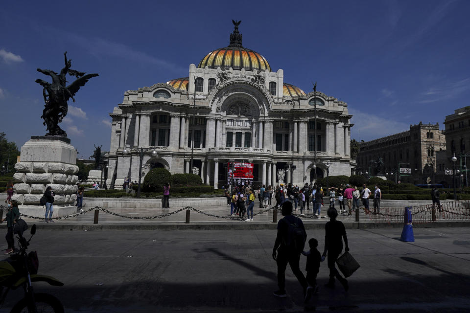 People walk outside the Palacio de Bellas Artes, Fine Arts Palace, in downtown Mexico City, Monday, Oct. 18, 2021. Starting Monday, Mexico City lifts some of its COVID-19 restrictions, allowing bars, clubs and indoor events to fill up to 50% capacity, while massive outdoor events can fill to capacity but masks will still be required. (AP Photo/Fernando Llano)