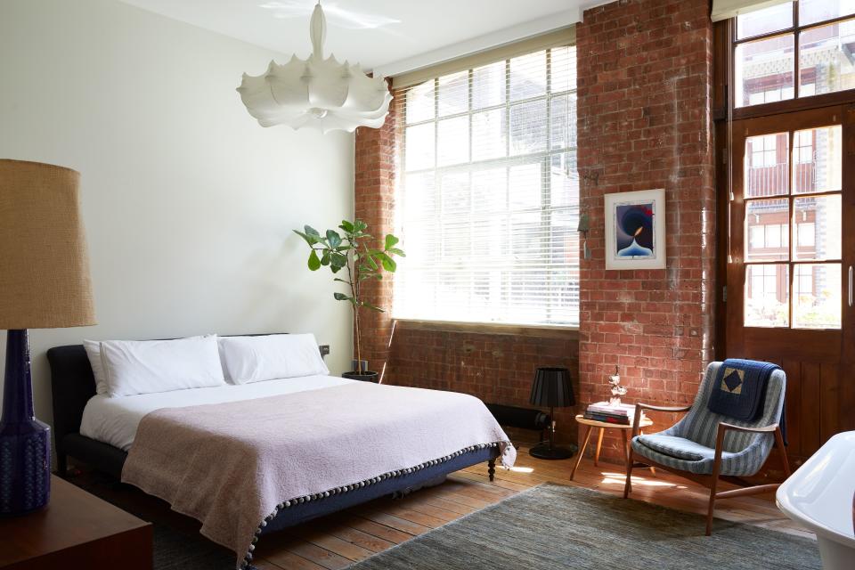 The bedroom looks onto a tranquil courtyard at the rear of the building. The bed is another piece by Tovey’s favorite furniture designer, Matthew Hilton. Above it hangs a Zeppelin light by Marcel Wanders. Tovey had the midcentury chair reupholstered in a Raf Simons for Kvadrat fabric, while the vintage light is from Shoreditch store, Atomic Antiques. The work above the table and chair is by New York painter Loie Hollowell.