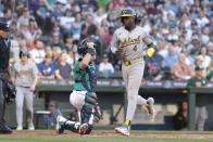 Oakland Athletics' Lawrence Butler (4) scores on a hit by Abraham Toro, next to Seattle Mariners catcher Cal Raleigh during the third inning of a baseball game Saturday, May 11, 2024, in Seattle. (AP Photo/Jason Redmond)
