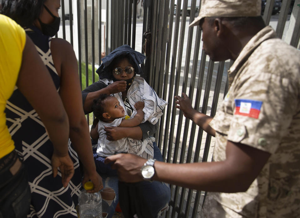 A Haitian police asks a woman to move away from a gate at the U.S. Embassy in Port-au-Prince, Haiti, Friday, July 9, 2021. A large crowd gathered outside the embassy amid rumors on radio and social media that the U.S. will be handing out exile and humanitarian visas, two days after Haitian President Jovenel Moise was assassinated in his home. (AP Photo/Joseph Odelyn)