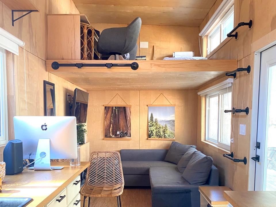 Interior of the tiny house with kitchen, gray couch, and loft up above