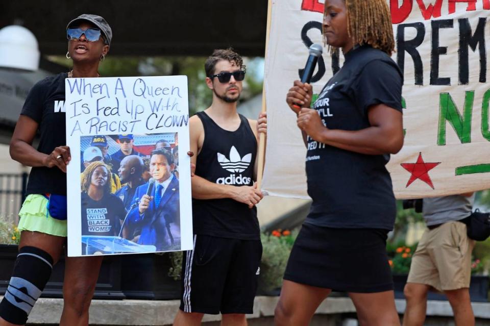 Sheila Jackson sostiene un cartel con una foto que muestra a la representante de la Florida Angie Nixon mirando fijamente al gobernador Ron DeSantis mientras la Angie Nixon real pasa al frente mientras habla el lunes 28 de agosto de 2023, en el James Weldon Johnson Park, en el downtown de Jacksonville, Florida. A la luz del reciente tiroteo en el Dollar General, que dejó tres personas negras muertas, cientos salieron a manifestarse contra la supremacía blanca.