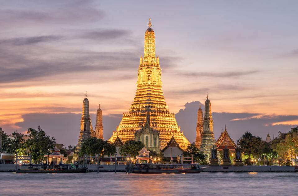 A majestic, ornate religious structure stands on the edge of the Chao Phraya River in Bangkok, Thailand