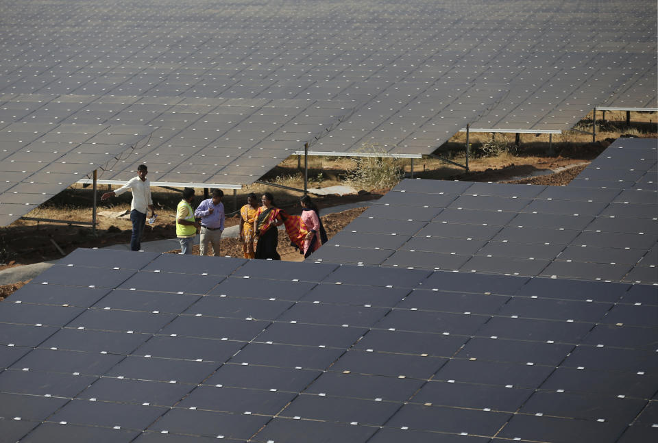 FILE - People stand between solar panels installed at the Pavagada Solar Park 175 kilometers (109 miles) north of Bangalore, India, Thursday, March 1, 2018. The Indian government will not consider any proposals for new coal plants for the next five years and focus on growing its renewables sector, according to an updated national electricity plan released Wednesday evening. (AP Photo/Aijaz Rahi, File)