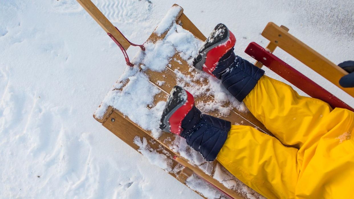 top view of a small child in snow gear and kids snow boots being pulled on a sled in the snow