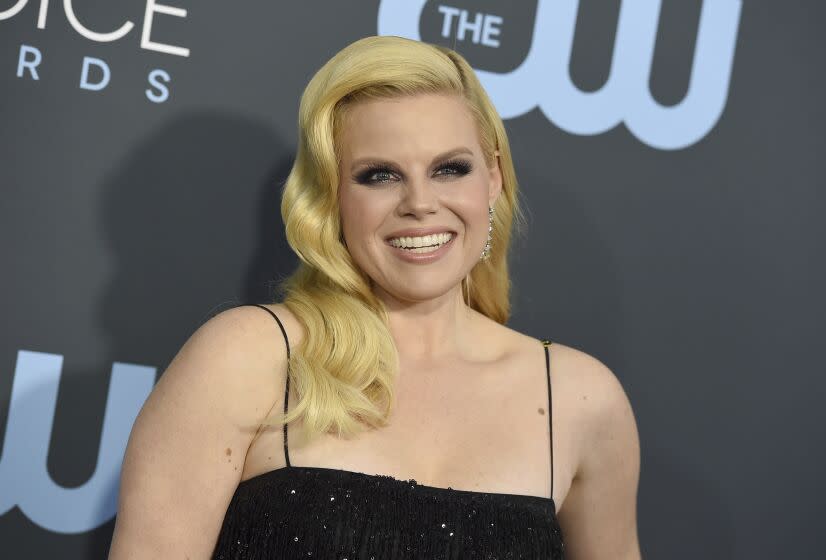 A woman with blonde hair over her shoulder wearing a black thin-strapped dress at a red carpet event