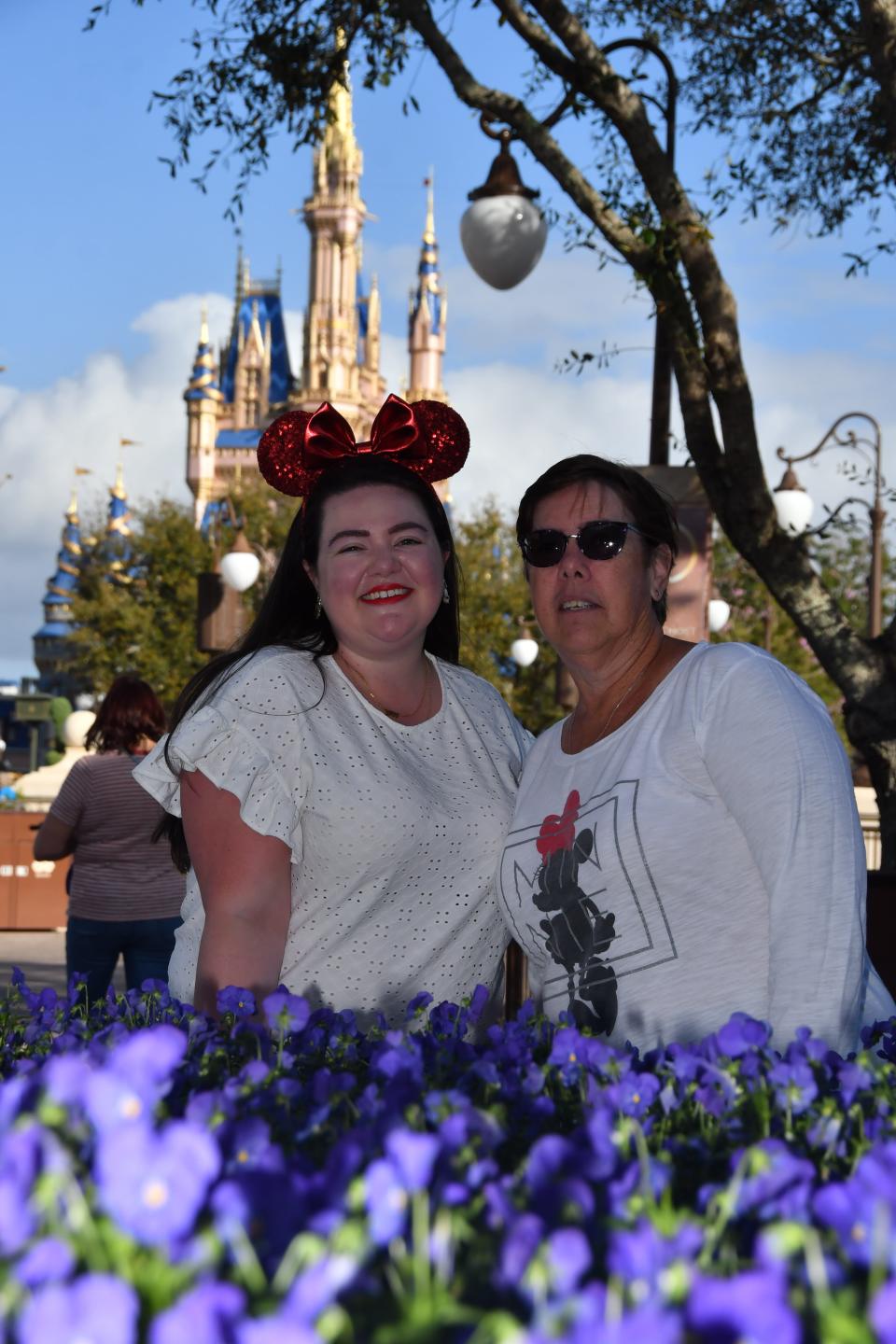 megan and her mom posing behind flowers at magic kingdom with the castle in the background