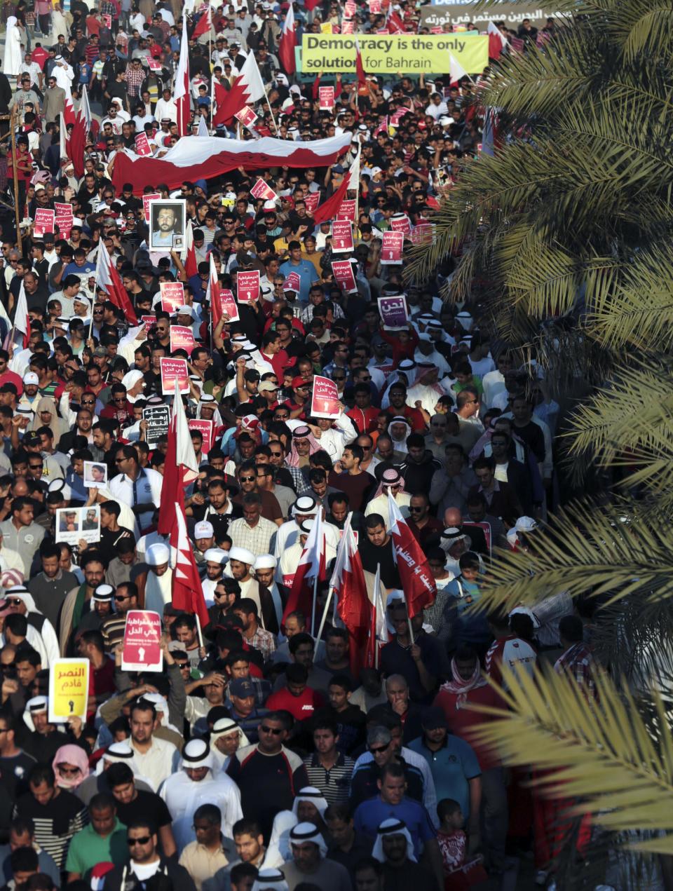 Tens of thousands of Bahraini pro-democracy protesters wave signs, pictures of prisoners and people killed in three years of unrest as well as national flags during a march along a divided four-lane highway near Barbar, Bahrain, west of the capital of Manama, on Saturday, Feb. 15, 2014. Protesters called for the long-serving prime minister, Sheik Khalifa bin Salman Al Khalifa, to step down and for democracy in the Gulf island kingdom. The yellow sign, lower left, reads, "victory is coming," and Arabic writing on most small red signs reads, "democracy is the solution." (AP Photo/Hasan Jamali)