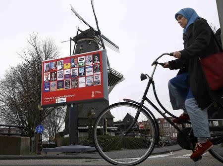 A woman cycles past an election poster billboard and a windmill , the day before a general election, in Amsterdam, Netherlands, March 14, 2017. REUTERS/Michael Kooren