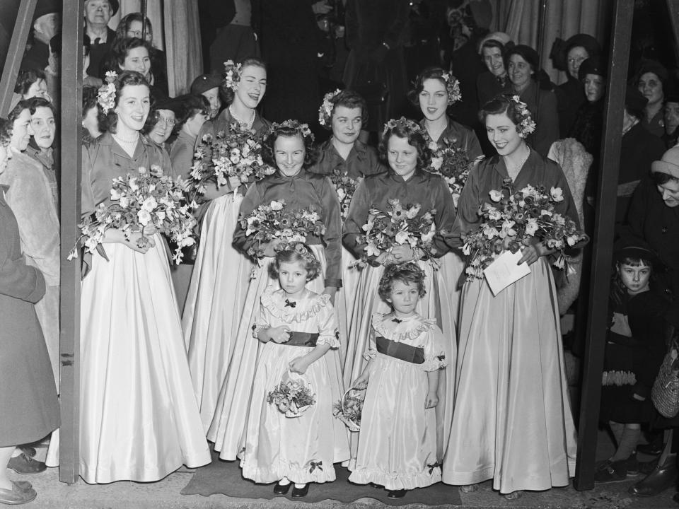 Camilla Duchess of Cornwall as a young bridal attendant. A group of women wear long gowns and hold bouquets.