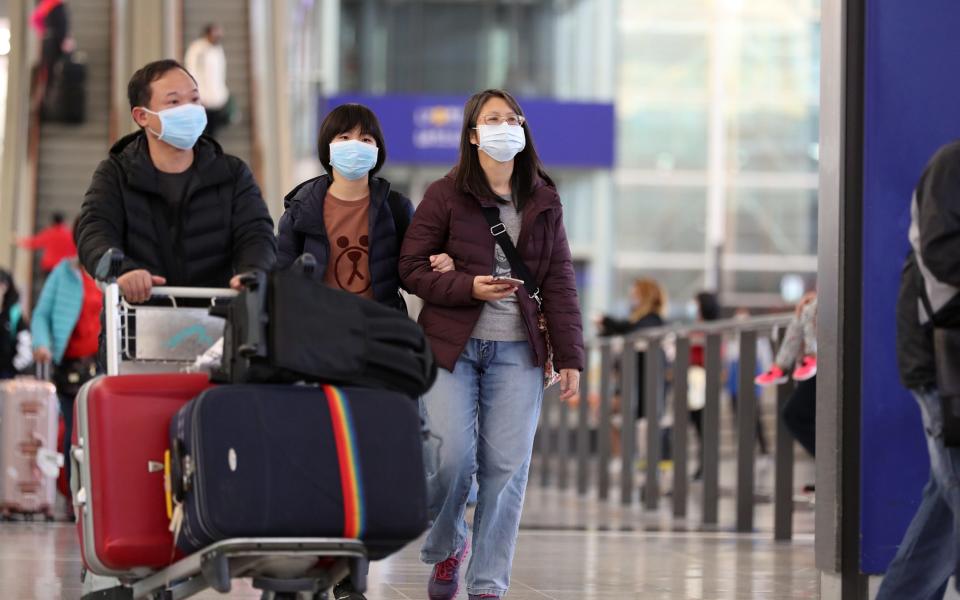 Travelers wearing face masks walk through the arrival hall at the Hong Kong International Airport in Hong Kong - Bloomberg
